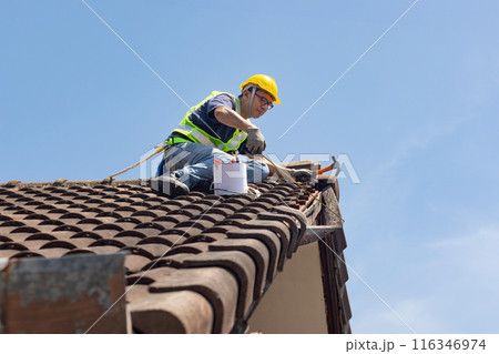 Worker man repairing eaves and tile of the old roof.. 116346974