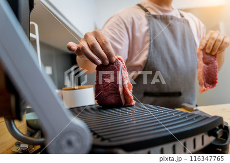 Chef at the kitchen preparing beef steaks on the home electric grill Chef at the kitchen preparing beef steaks on the home electric grill 116347765