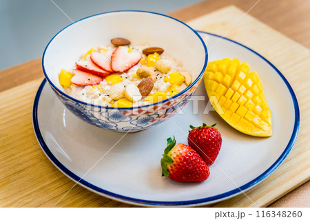 A bowl of oats with strawberries and mango arranged on a plate A bowl of oats with strawberries and mango arranged on a plate 116348260