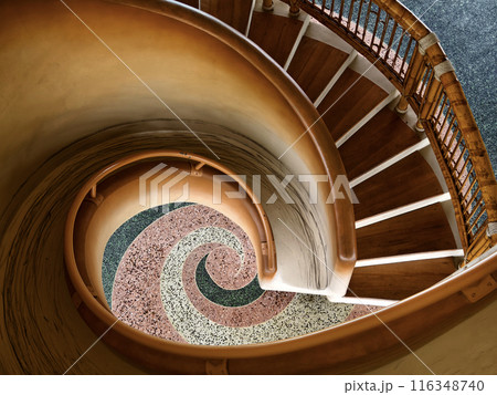 There is a spiral staircase in a building with a wooden railing 116348740
