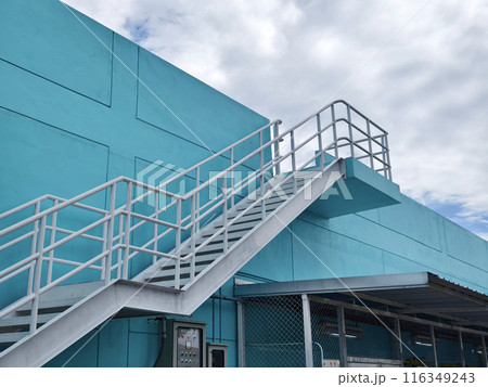 Metal stairs to blue building against sky and clouds 116349243