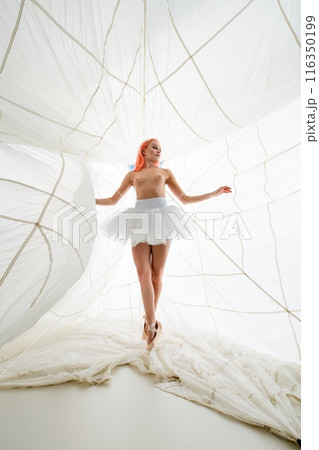 Woman in White Tulle Skirt Posing in a White Fabric Structure 116350199