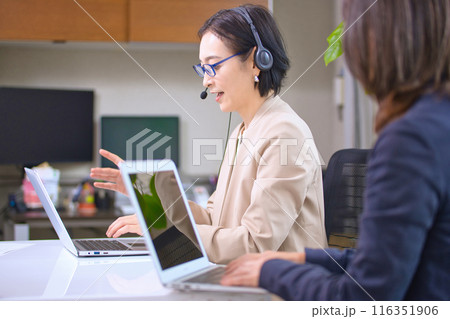 オフィスでヘッドセットをつけて仕事するミドル女性 116351906