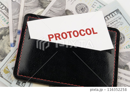 Business concept. Text PROTOCOL is written on a business card in a black leather accessory against the background of American dollars 116352258