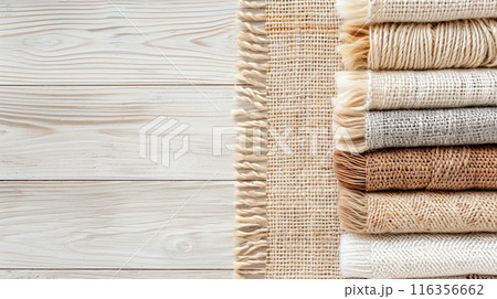 Neatly stacked beige fabrics on a wooden surface, showcasing natural textures and neutral tones for a cozy ambiance. 116356662