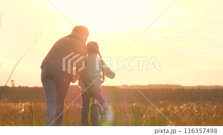 Woman teaching girl to ride bike, silhouettes at sunrise. Exciting activities with family, older, mom and daughter spend time together. Playful interesting form of learning to ride bike. Fun childhood 116357498