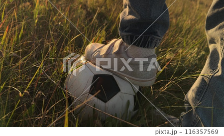 Child foot in field kicks ball playing football. Close up foot of teenage boy kid with soccer ball. Child kid at sunset in field kicking ball playing football alone enjoying football soccer game. 116357569