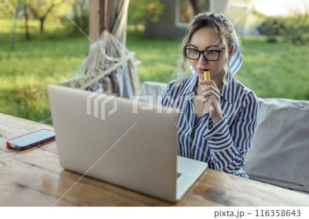 freelance girl works at a computer and smokes an electrode cigarette outside the house  116358643
