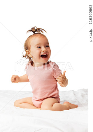 Vertical image of happy laughing little baby girl, child in pink bodysuit sitting on bed and smiling isolated on white background 116360662