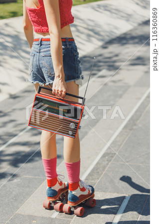 Cropped photo of skater girl, dressed in vibrant summer attire, holds retro radio and listening music, while roller skating in park. Cropped photo of skater girl, dressed in vibrant summer attire, holds retro radio and listening music, while roller skating in park. 116360869