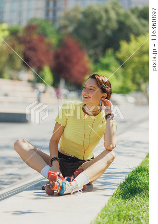 Energetic and joyful skater girl enjoying sunny park break, sitting on concrete ramp, wearing yellow crop top and brown shorts. Energetic and joyful skater girl enjoying sunny park break, sitting on concrete ramp, wearing yellow crop top and brown shorts. 116360897