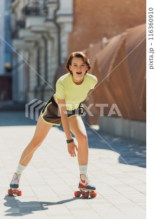Happy, athlete teenage girl in vibrant sports attire roller skating in motion on tree-lined urban street. Dynamic photo. 116360910