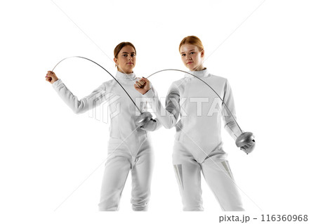 Two female fencers pose confidently with their swords, showcasing their skills and precision against white studio background. Two female fencers pose confidently with their swords, showcasing their skills and precision against white studio background. 116360968