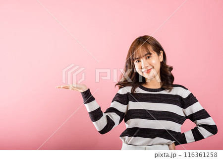 Asian happy portrait beautiful cute young woman smile standing presenting product holding something on palm away side, studio shot isolated on pink background with copy space, female show hand gesture 116361258