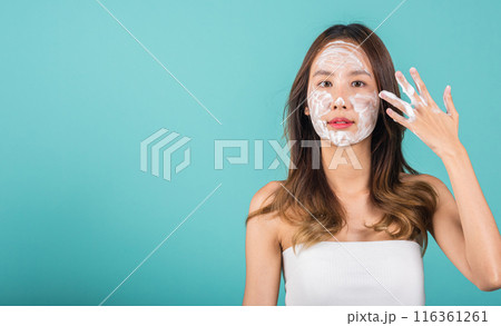 Asian woman face wash exfoliation scrub soap with skincare cleansing, Portrait beautiful female smile applies foaming cleanser healthy skin, Studio isolated on blue background, skincare daily routine 116361261