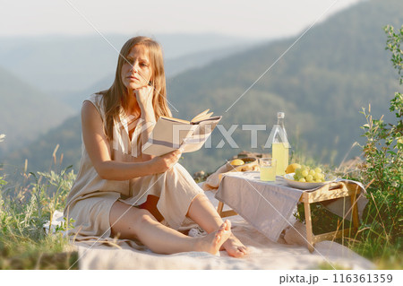 A woman is enjoying a peaceful moment reading a book during a relaxing outdoor picnic in nature A woman is enjoying a peaceful moment reading a book during a relaxing outdoor picnic in nature 116361359