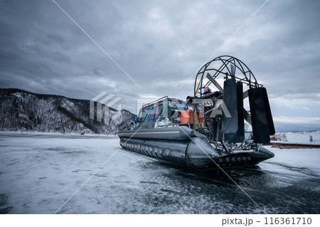 An airboat is cruising on a frozen lake in the winter season amidst a snowy landscape An airboat is cruising on a frozen lake in the winter season amidst a snowy landscape 116361710
