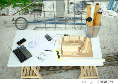 Top view Architectural house model, laptop and blueprints on table at construction site 116361741