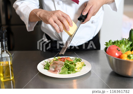 厨房でグレーターでチーズを削る調理師の手元 116361782
