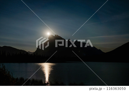 Moonrise at Vermilion Lakes in summer night. Banff National Park, Canadian Rockies, Alberta, Canada. Bright full moon over Mount Rundle and light up the night with golden reflection on lake surface. Moonrise at Vermilion Lakes in summer night. Banff National Park, Canadian Rockies, Alberta, Canada. Bright full moon over Mount Rundle and light up the night with golden reflection on lake surface. 116363050