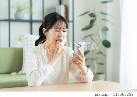 リビングでスマホを見る若い女性 116365252