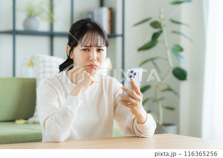 リビングでスマホを見る若い女性 116365256