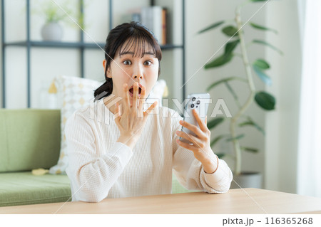 リビングでスマホを見る若い女性 116365268