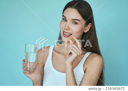 Woman Holding Vitamin Capsule And Glass Of Water On Blue Background Woman Holding Vitamin Capsule And Glass Of Water On Blue Background 116365672