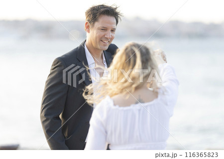 A man and a woman are standing on a beach, smiling at each other 116365823