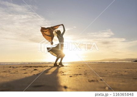 A woman stands on a beach with a scarf around her neck 116365848