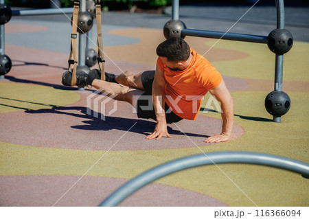 Athletic man sportswear placing feet on trx straps, doing plank exercises, growing strength. Outdoor trx workout Athletic man sportswear placing feet on trx straps, doing plank exercises, growing strength. Outdoor trx workout 116366094