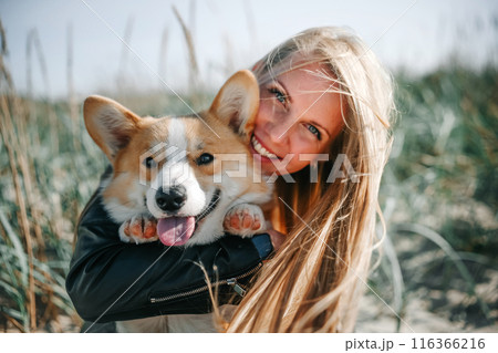 Happy Woman Holding a Smiling Corgi on a Sunny Day 116366216