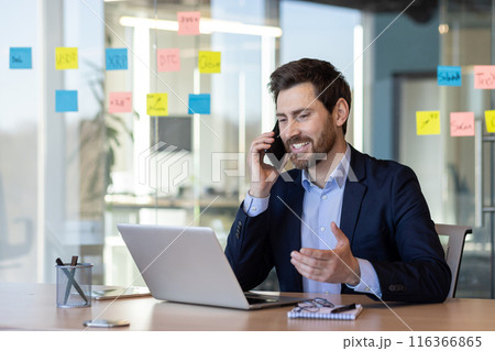 Smiling happy boss talking on the phone, businessman satisfied with the results of negotiations achieved at the workplace inside the office, mature boss in a business suit working with a laptop. Smiling happy boss talking on the phone, businessman satisfied with the results of negotiations achieved at the workplace inside the office, mature boss in a business suit working with a laptop. 116366865
