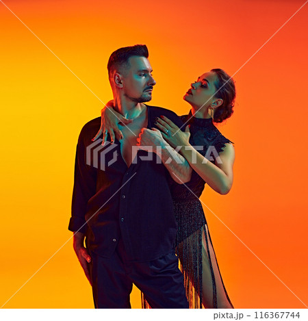 Portrait of handsome man and beautiful woman, passionate couple dancing bachata against gradient yellow orange background in neon light 116367744