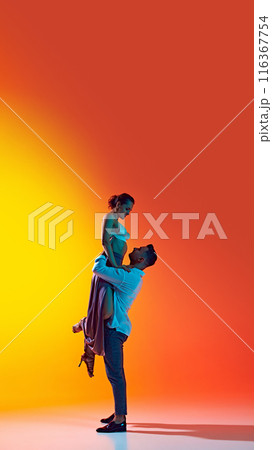 Vertical full-length image of artistic and talented young couple, man and woman dancing bachata against gradient yellow orange background in neon light Vertical full-length image of artistic and talented young couple, man and woman dancing bachata against gradient yellow orange background in neon light 116367754