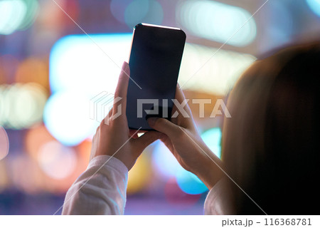 夜の繁華街でスマートフォンをかざす若い女性 116368781