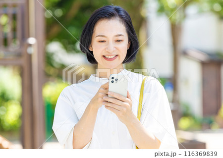 新緑の中でスマホを見るミドル女性 116369839