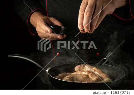 Chef adds spices to a frying pan with meat sausage by hand. Cooking or frying sausage in a restaurant or cafe kitchen 116370715