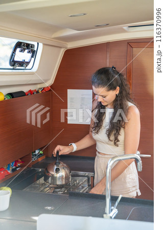 Young woman standing and preparing tea in kitchen in cabin of modern yacht during sailing in sea. Yacht life concept Young woman standing and preparing tea in kitchen in cabin of modern yacht during sailing in sea. Yacht life concept 116370996