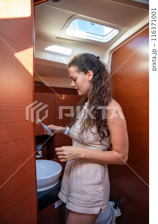 Young Woman brushing her teeth with an electric brush in bathroom of a yacht during sailing in sea. Yacht life concept. Trip around the world 116371001