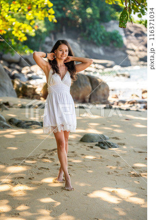 Stylish attractive young woman wearing in white dress having fun on on seashore in the shade of trees and palms, freedom and happiness 116371034