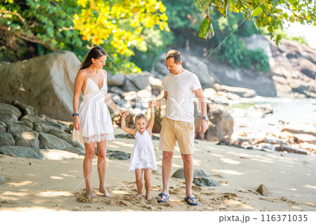 Happy young family of three taking a walk on the beach, having a fun on seashore in the shade of trees and palms. Happy family concept. Happy young family of three taking a walk on the beach, having a fun on seashore in the shade of trees and palms. Happy family concept. 116371035