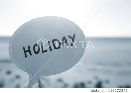 Stick with paper speech bubble with words Holiday on background blue sea, sky, sandy beach on sunny summer day. Text-balloons with text from letters. Concept, symbol, sign vacation travel. Blue color Stick with paper speech bubble with words Holiday on background blue sea, sky, sandy beach on sunny summer day. Text-balloons with text from letters. Concept, symbol, sign vacation travel. Blue color 116372341