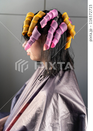 A woman in a salon cape with her hair in pink and yellow curlers A woman in a salon cape with her hair in pink and yellow curlers 116372715