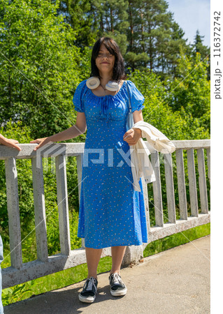 Woman in blue dress on bridge, holding white jacket, surrounded by greenery 116372742
