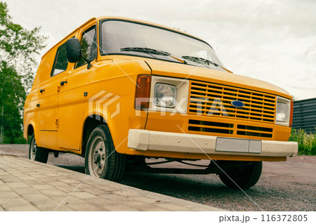 A yellow van is parked on a sidewalk in a city setting 116372805
