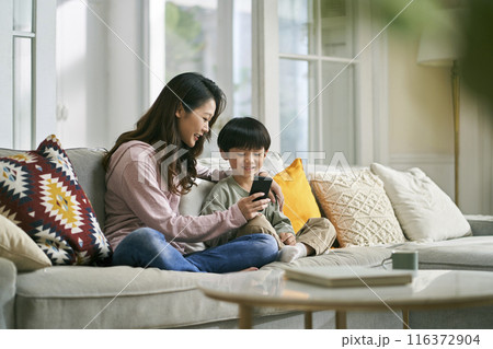 young asian mother sharing cellphone pictures with son at home 116372904
