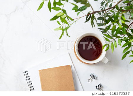 A cup of tea and craft notepad on a light marble background with green branches close-up A cup of tea and craft notepad on a light marble background with green branches close-up 116373527