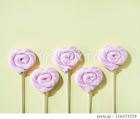 Pink lollipops in the shape of hearts on a yellow background. Top view and copy space Pink lollipops in the shape of hearts on a yellow background. Top view and copy space 116373579