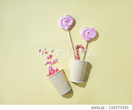 Pink lollipops in the shape of hearts at paper cup with color sugar on a yellow background. Pink lollipops in the shape of hearts at paper cup with color sugar on a yellow background. 116373585
